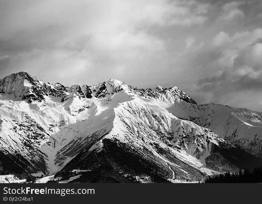 Snowy winter mountain and cloudy sky in evening. Caucasus Mountains. Svaneti region of Georgia. Black and white toned landscape. Snowy winter mountain and cloudy sky in evening. Caucasus Mountains. Svaneti region of Georgia. Black and white toned landscape.