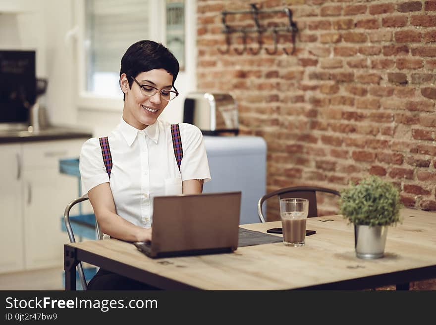 Spain, Madrid, Madrid. Young woman with very short haircut and eyeglasses typing with a laptop at home. Working at home concept.