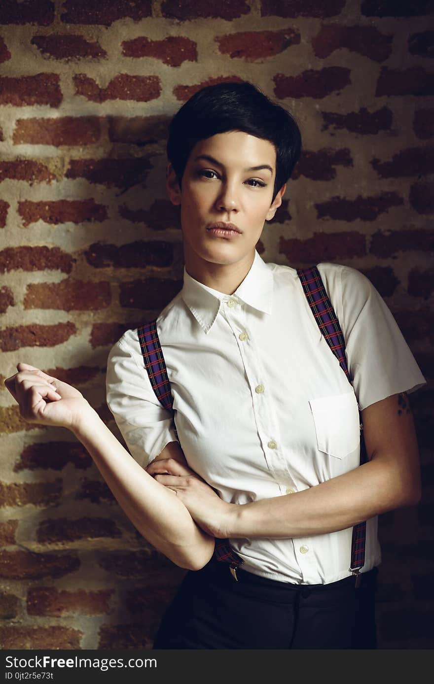 Beautiful young woman, model of fashion, with very short haircut, looking at camera with a brick wall in the background. Beauty and hairstyles concept. Beautiful young woman, model of fashion, with very short haircut, looking at camera with a brick wall in the background. Beauty and hairstyles concept.