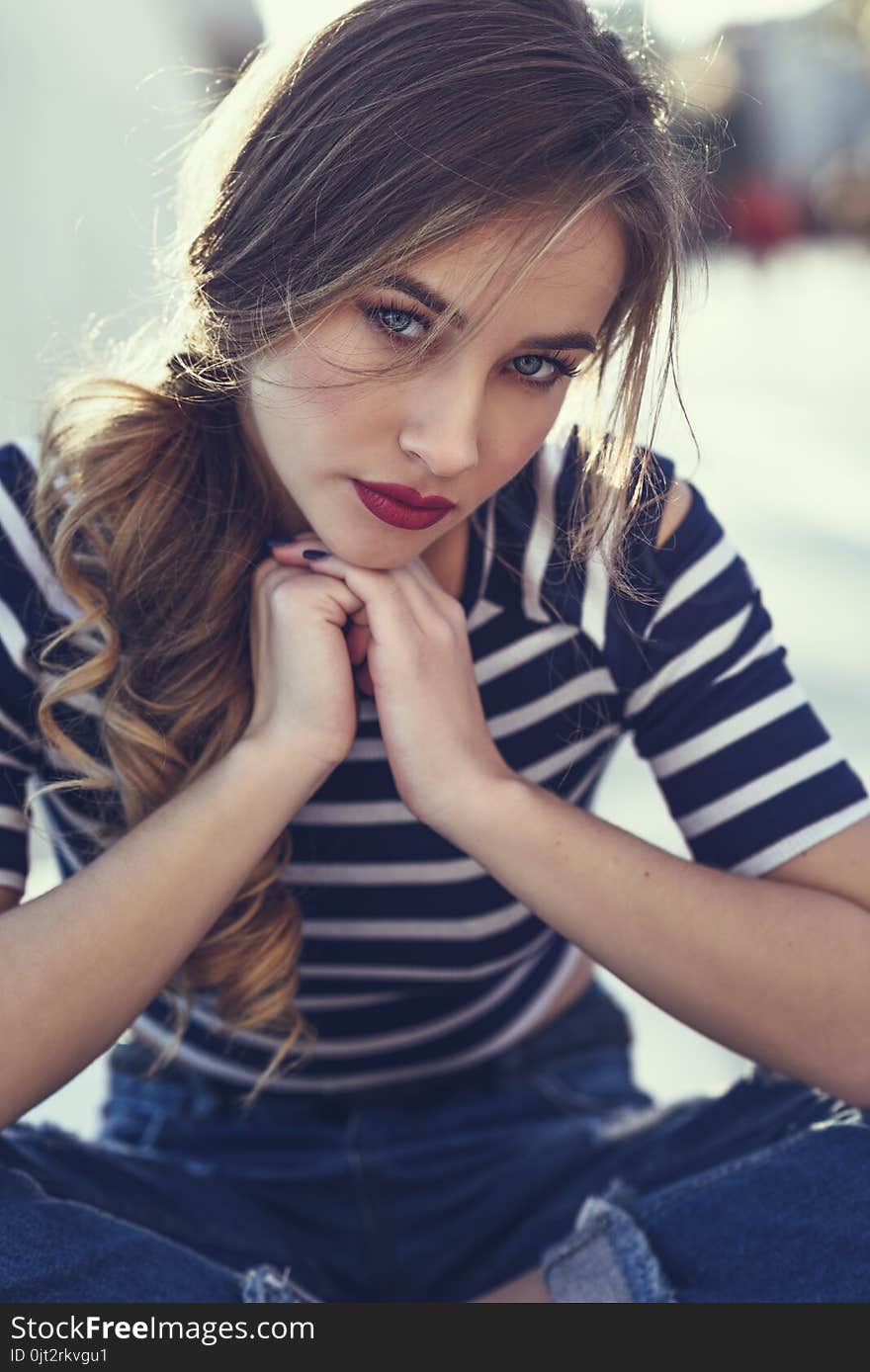 Blonde woman, model of fashion, sitting in urban background.