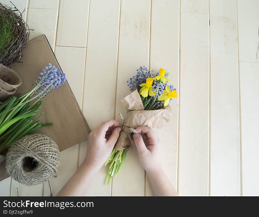 Children`s hands collect a bouquet as a gift. A gift for mom. Spring festive bouquet in a crafting package. Pruning flowers. The child is a florist. Wooden background. Field bouquet. Eco-style.