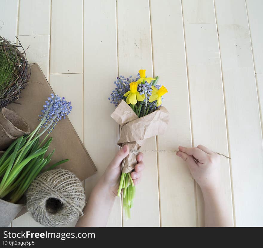 Children`s hands collect a bouquet as a gift. A gift for mom. Spring festive bouquet in a crafting package. Pruning flowers. The child is a florist. Wooden background. Field bouquet. Eco-style.