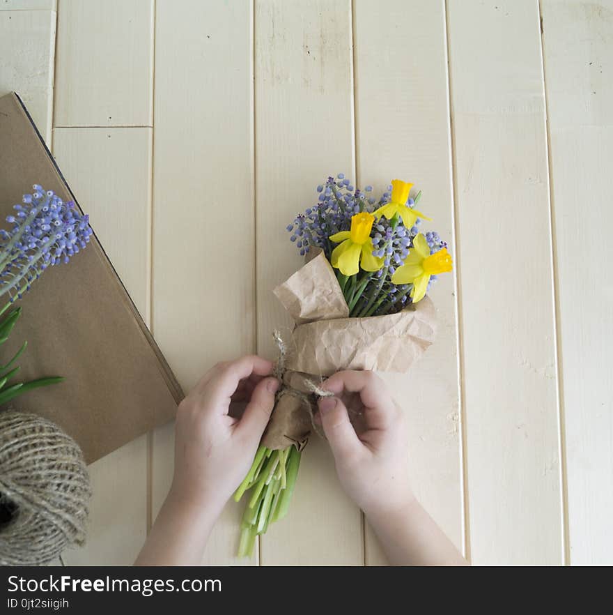 Children`s hands collect a bouquet as a gift. A gift for mom. Spring festive bouquet in a crafting package. Pruning flowers. The child is a florist. Wooden background. Field bouquet. Eco-style.