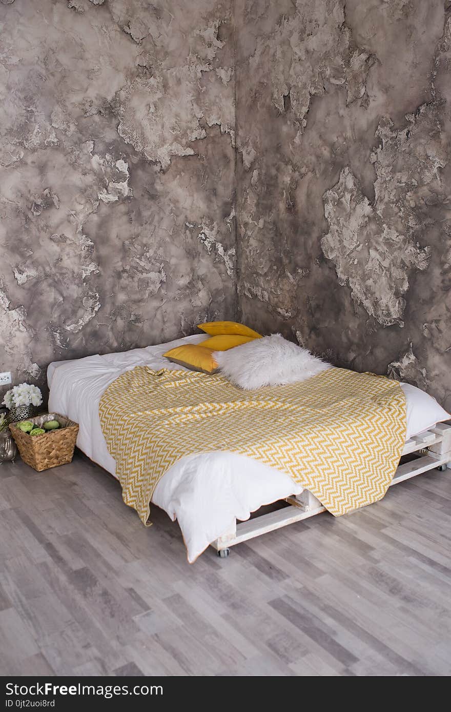 A loft style bedroom with recycled pallet bed. White and yellow bedding on bed with bedhead in loft bedroom interior. Loft