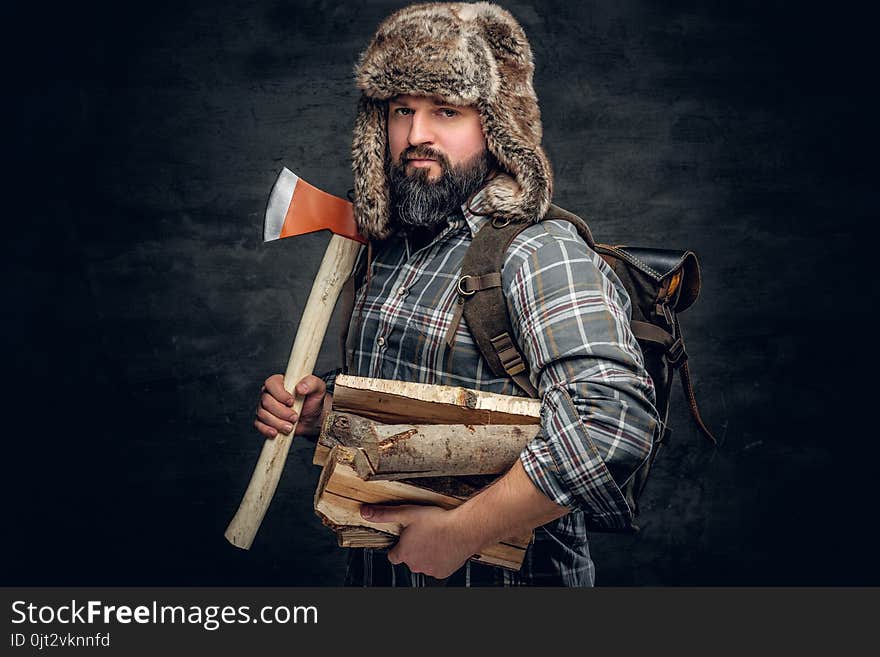 Portrait of brutal bearded hunter male dressed in a fleece shirt and a hat from a fur holds an axe on his shoulder. Portrait of brutal bearded hunter male dressed in a fleece shirt and a hat from a fur holds an axe on his shoulder.