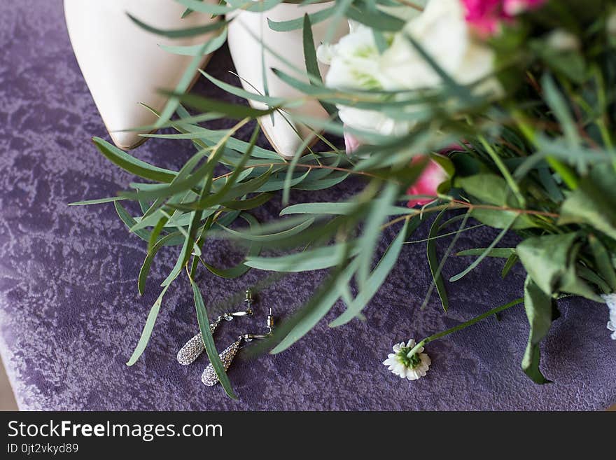 Wedding beige shoes and a bridal earring with gemstones lying on the lilac background. Wedding accessories.