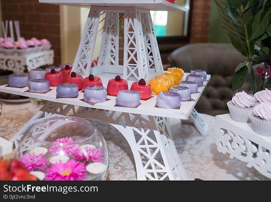 A tray with pink, orange and lilac little cakes. Candy bar. A lot of sweets at the wedding banquet.