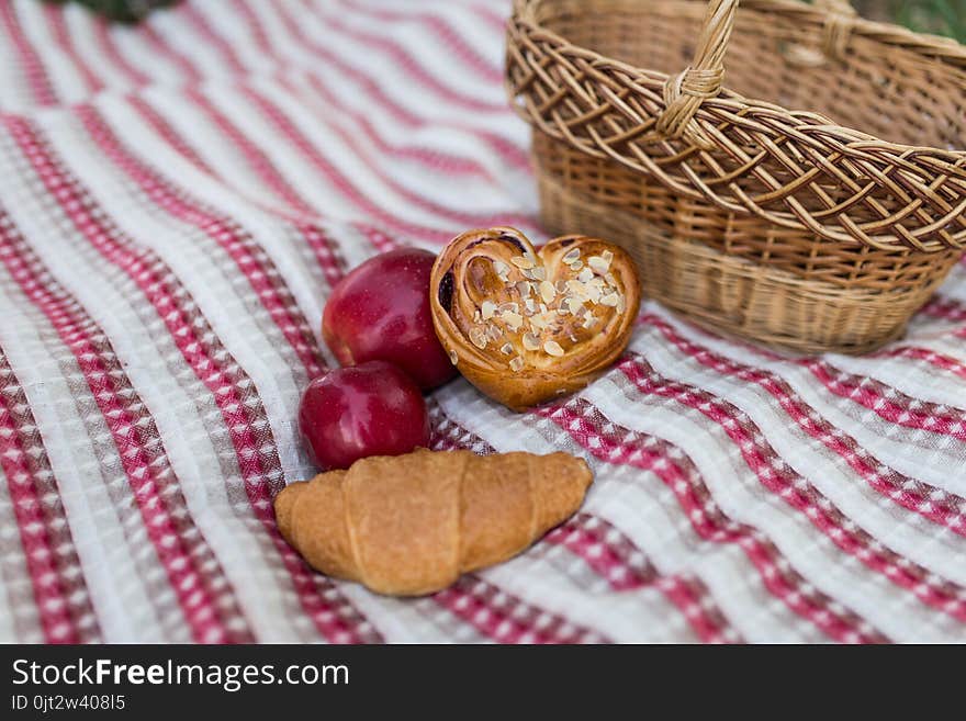 Romantic picnic in the garden - a basket with bakery and apples. Picnic on the lawn. Objects for picnic on a coverlet. Weekend.