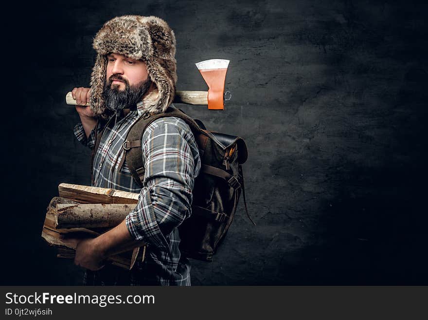 Portrait of brutal bearded hunter male dressed in a fleece shirt and a hat from a fur holds an axe on his shoulder. Portrait of brutal bearded hunter male dressed in a fleece shirt and a hat from a fur holds an axe on his shoulder.