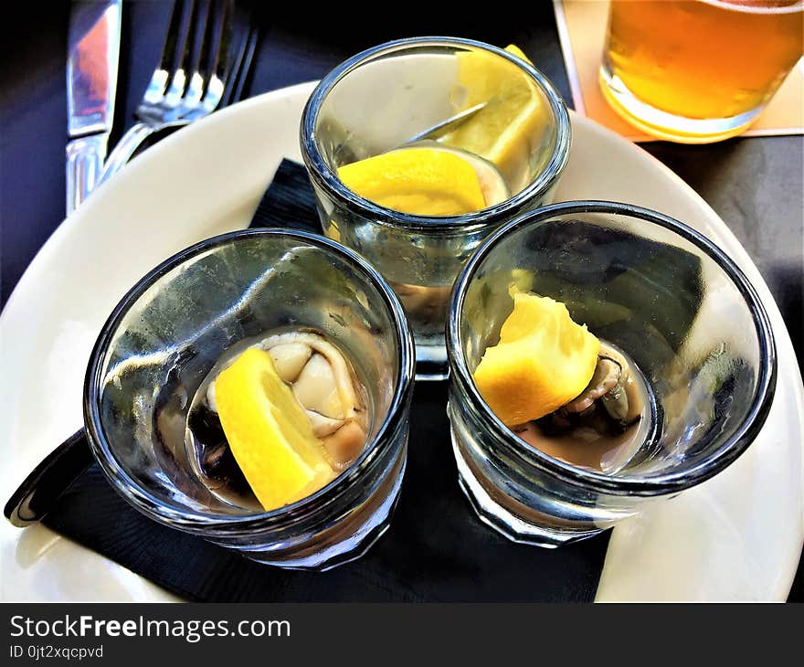 Three Oyster Shooters with Lemon in shot glasses, o a white plate, with a glass of beer