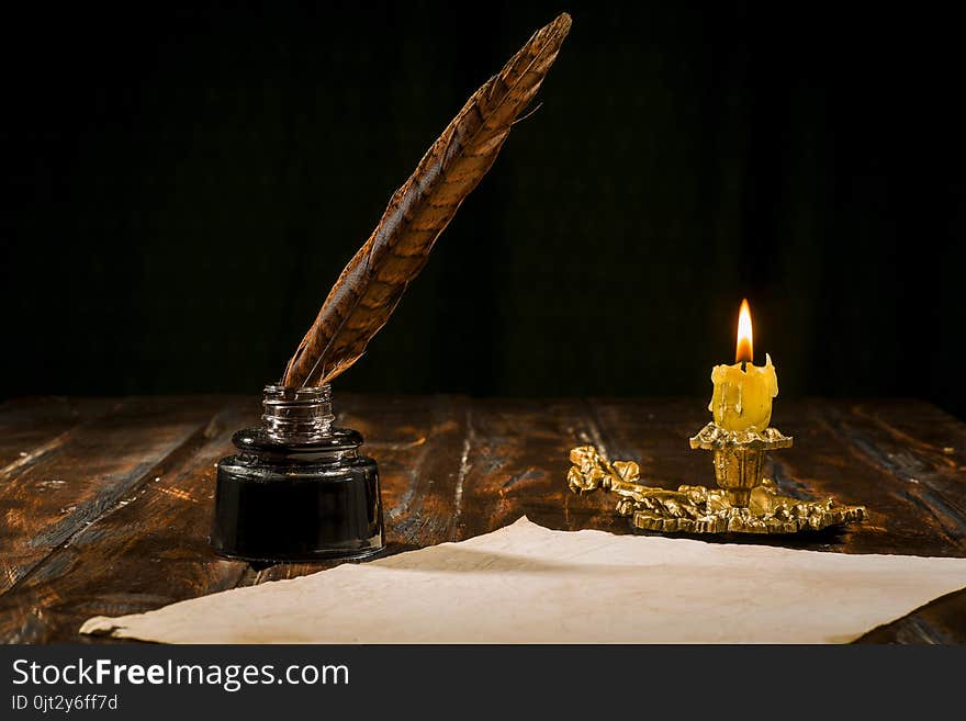 Education and writing concept, pen in ink bottle and candlestick with candle on wooden table on dark background. Education and writing concept, pen in ink bottle and candlestick with candle on wooden table on dark background.