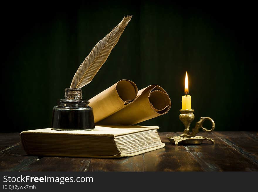 Education and writing concept, pen in ink bottle and candlestick with candle on wooden table on dark background. Education and writing concept, pen in ink bottle and candlestick with candle on wooden table on dark background.