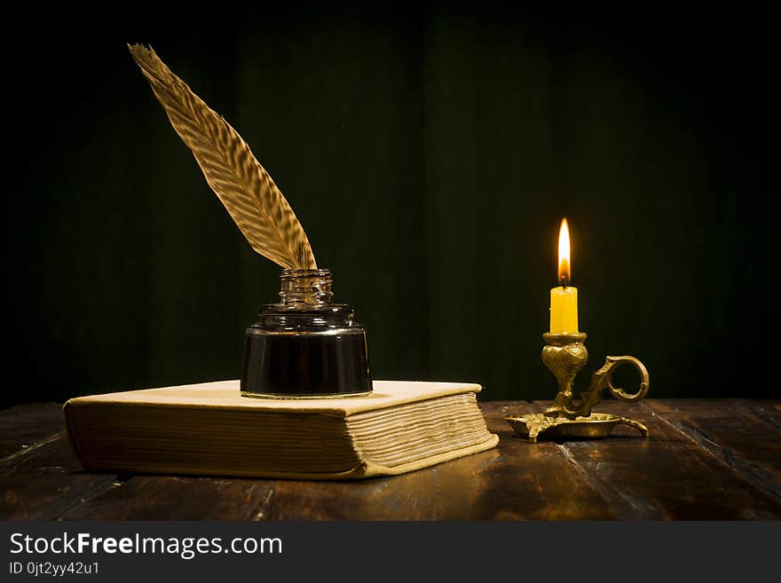 Education and writing concept, pen in ink bottle and candlestick with candle on wooden table on dark background. Education and writing concept, pen in ink bottle and candlestick with candle on wooden table on dark background.