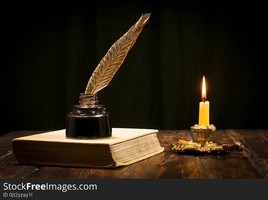 Education and writing concept, pen in ink bottle and candlestick with candle on wooden table on dark background. Education and writing concept, pen in ink bottle and candlestick with candle on wooden table on dark background.