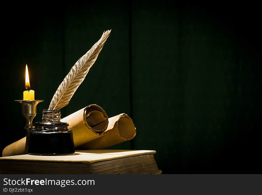 The concept of education and writing, a pen in an inkwell and a candle with a candle, and a book on a dark background.