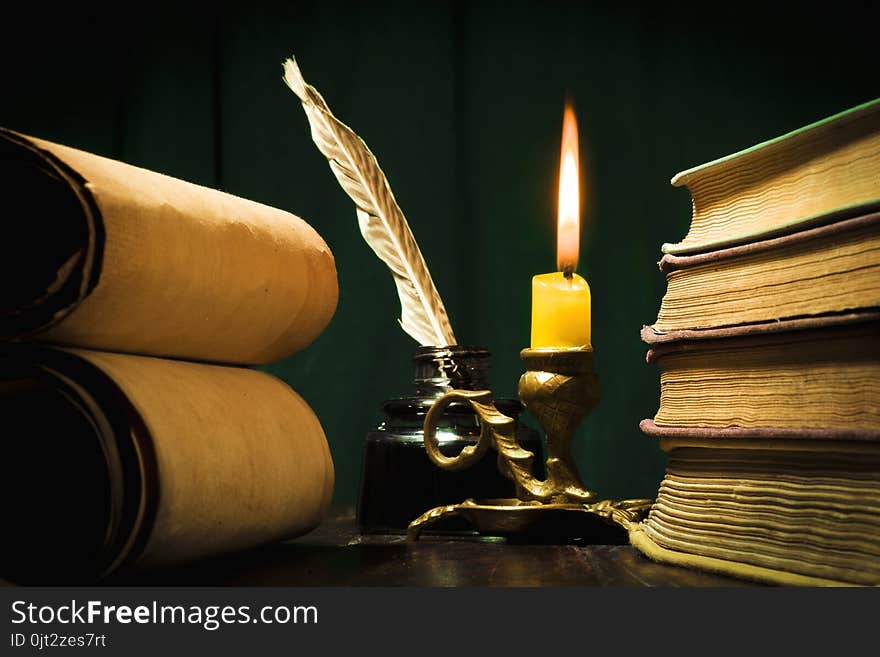 Concept of education and writing, a pen in an inkwell and a candle with a candle and scrolls of papyrus on a green background. Concept of education and writing, a pen in an inkwell and a candle with a candle and scrolls of papyrus on a green background