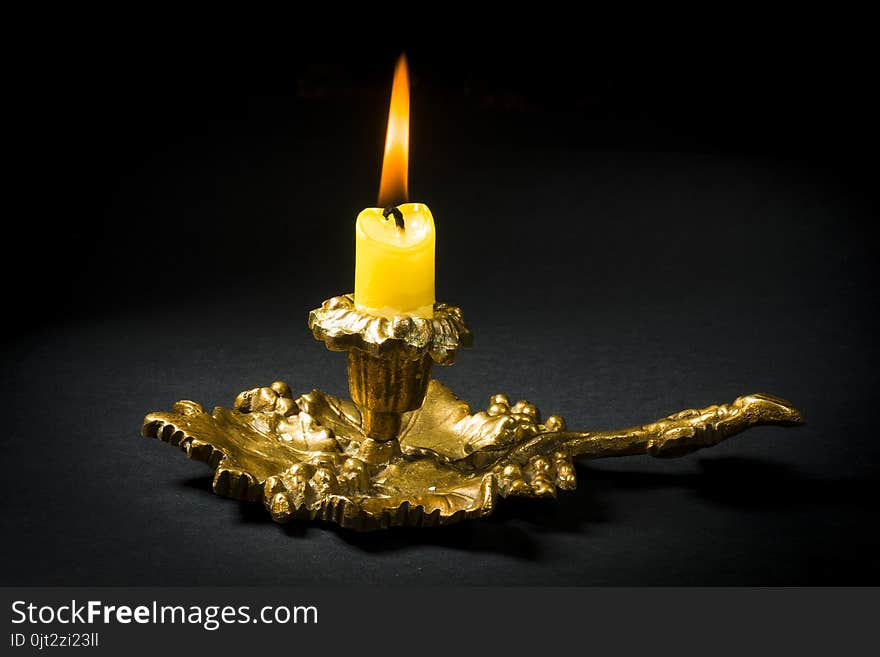 Vintage candlestick with a lit yellow candle on a black background