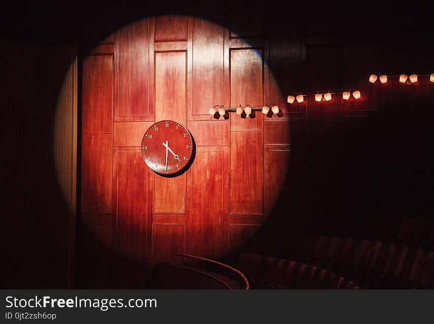 Wooden watch on a wood panel covered wall lit by a stage light showing half past four