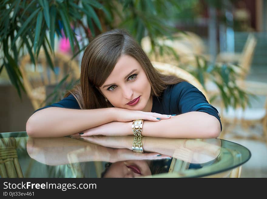 Pensive pretty girl leaning elbows on glass table in cafe. Pensive pretty girl leaning elbows on glass table in cafe