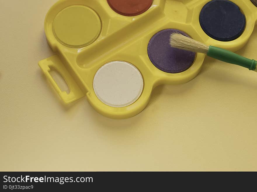 Watercolors in bright yellow box with big brush for kids are on the table . Kids art concept. Watercolors in bright yellow box with big brush for kids are on the table . Kids art concept.