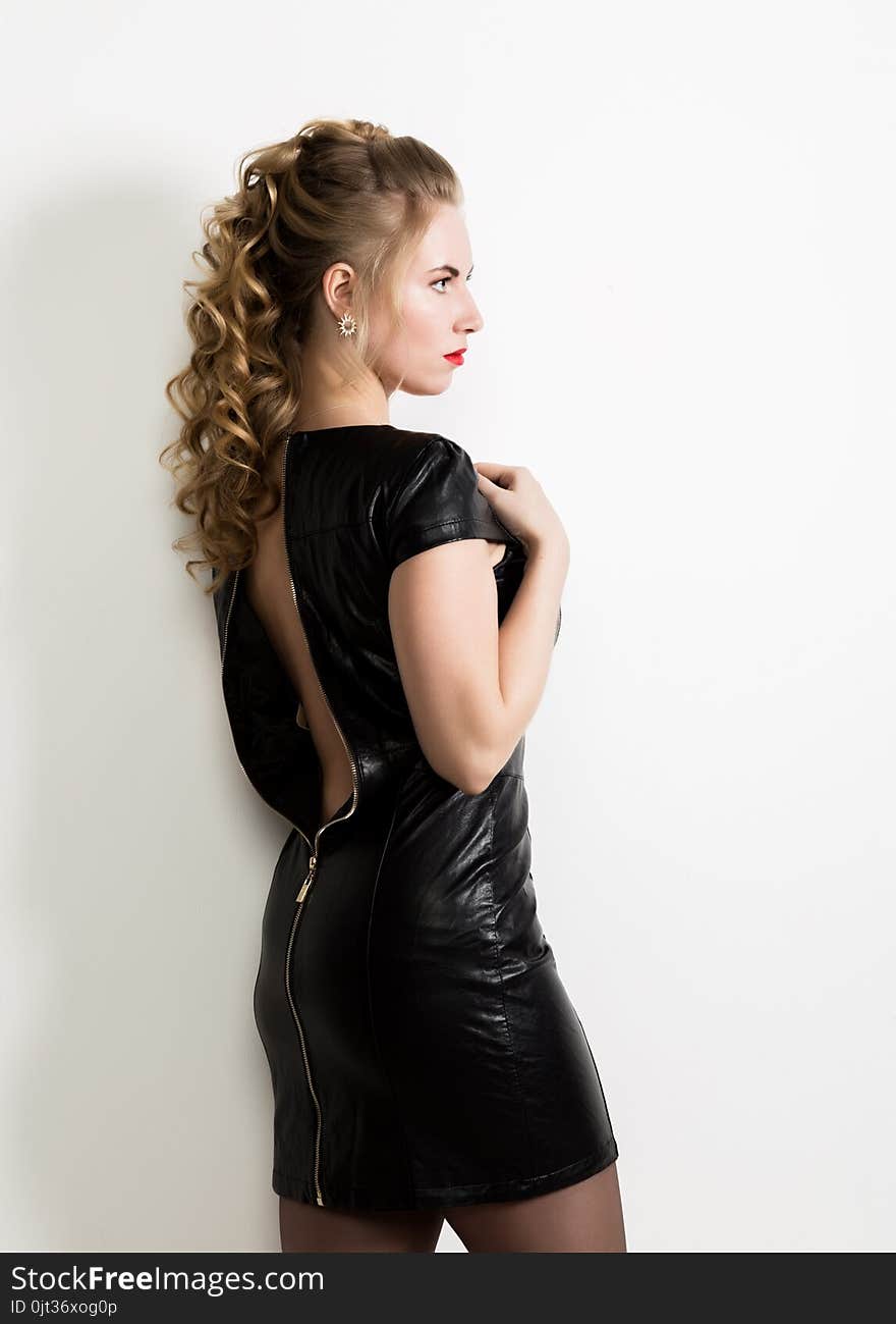 Beautiful Young Woman Wearing Short Leather Black Dress With Naked Back On A Light Background