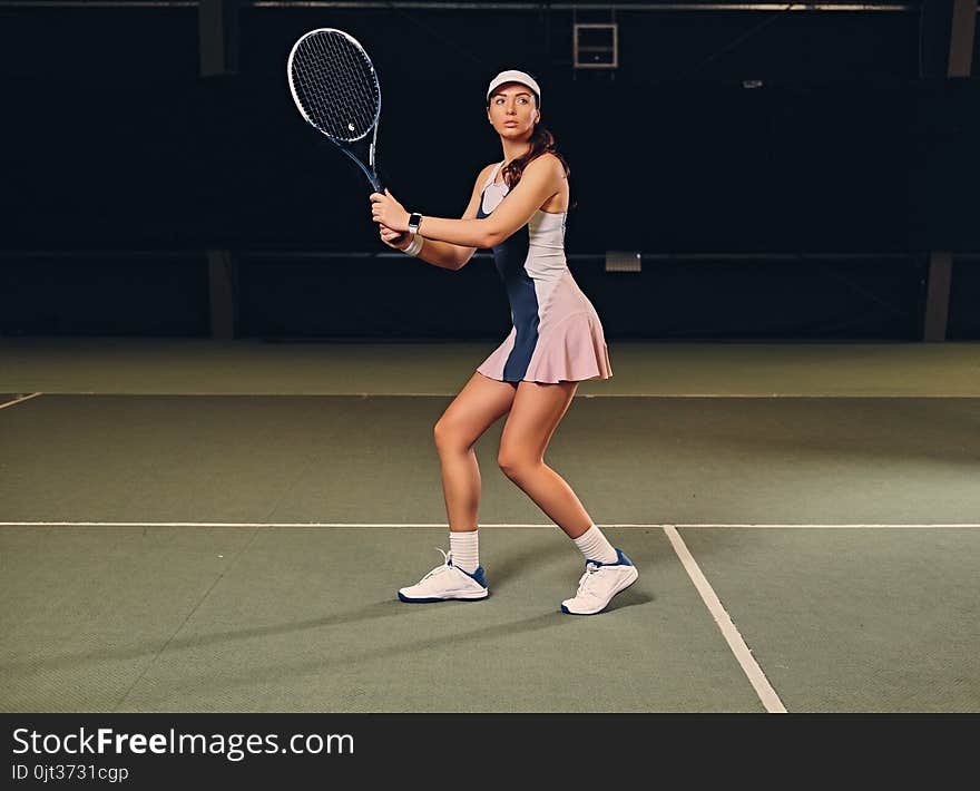 Female tennis player in action in a tennis court indoor.