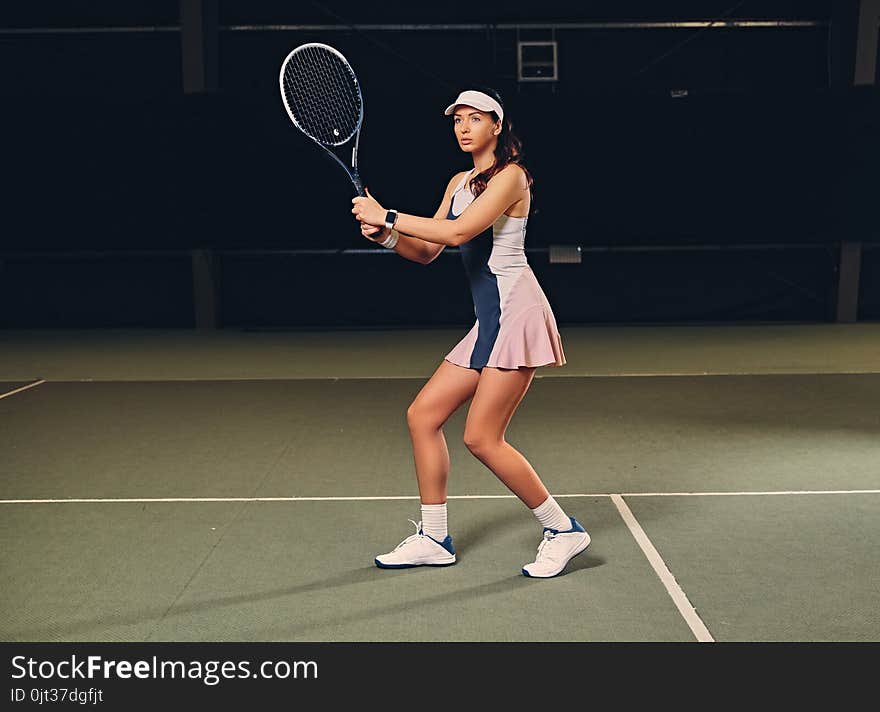 Female tennis player in action in a tennis court indoor.