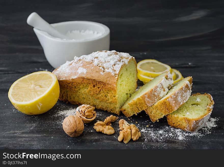 Mint cake on black surface with lemon, nuts, powdered sugar.