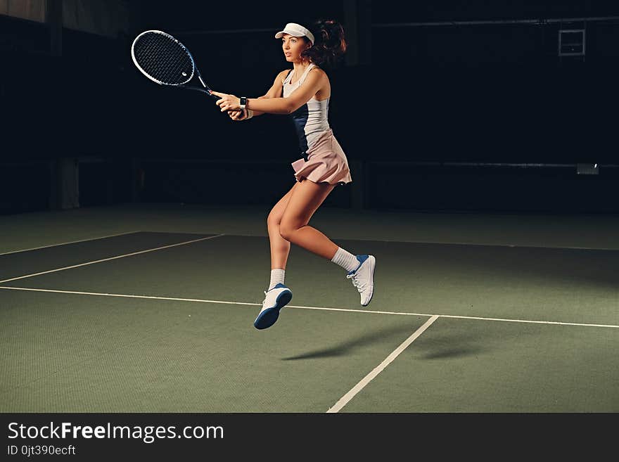 Female tennis player in action in a tennis court indoor.