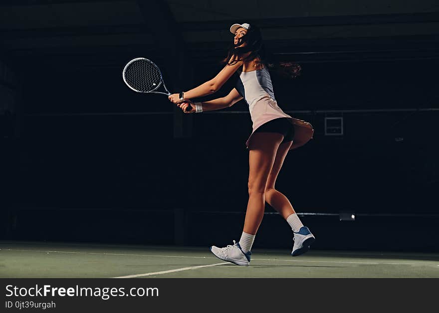 Female tennis player in action in a tennis court indoor.