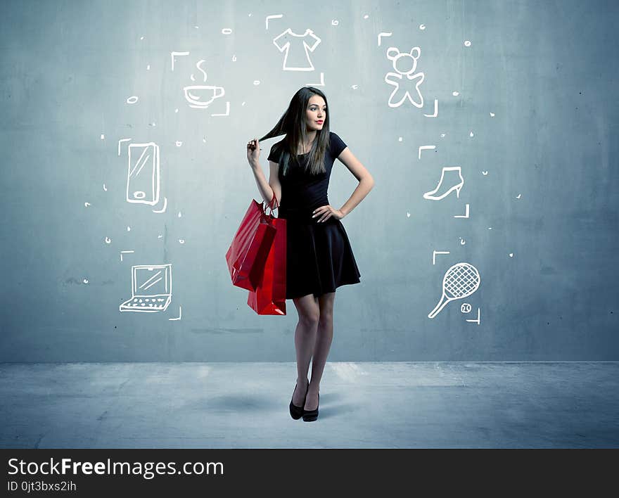 A beautiful young girl in black standing with red shopping bags in front of urban wall background and laptop, shoes, tennis icons concept. A beautiful young girl in black standing with red shopping bags in front of urban wall background and laptop, shoes, tennis icons concept