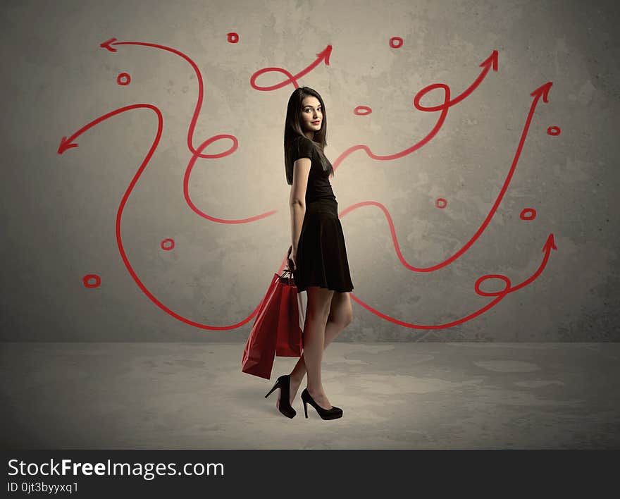 An elegant young lady in black holding red shopping bags in front of urban wall background with drawn red arrows and circles concept. An elegant young lady in black holding red shopping bags in front of urban wall background with drawn red arrows and circles concept