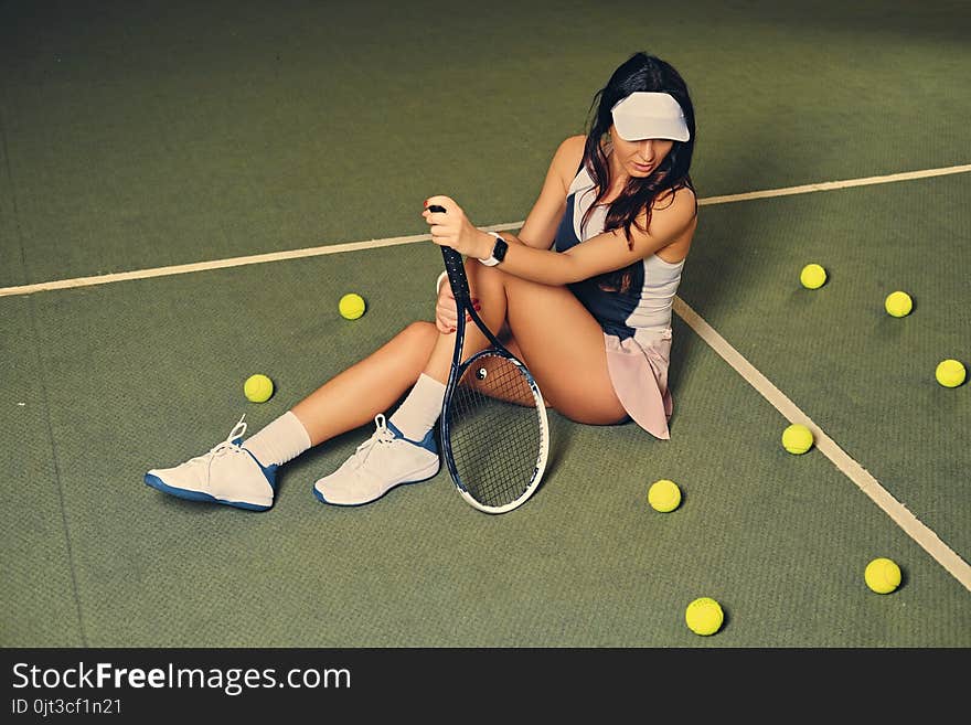 Female tennis player sits in a court and holds playing rocket.