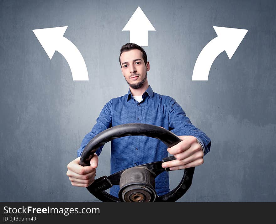 Young man holding black steering wheel with three arrows above his head pointing in different directions. Young man holding black steering wheel with three arrows above his head pointing in different directions