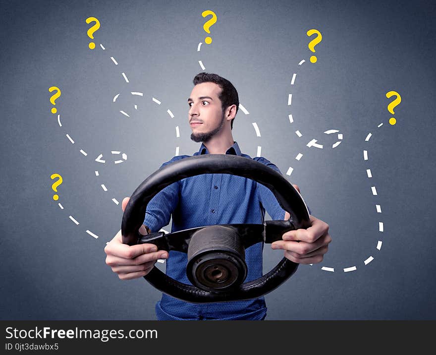 Young man holding black steering wheel with question marks around him. Young man holding black steering wheel with question marks around him