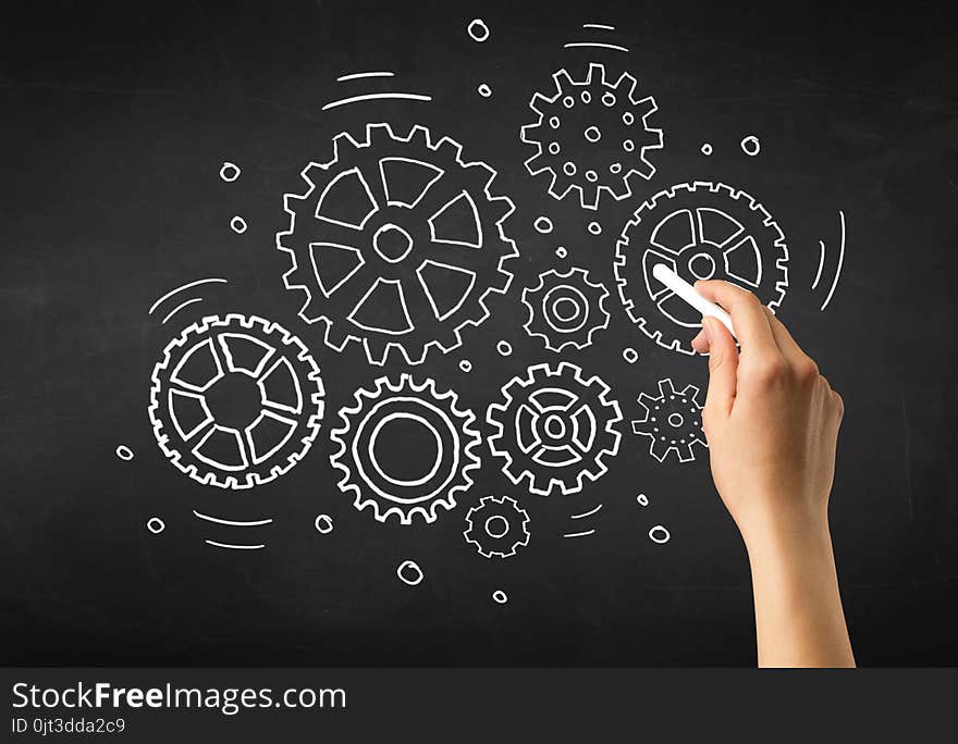 Female hand holding white chalk in front of a blackboard with gears drawn on it. Female hand holding white chalk in front of a blackboard with gears drawn on it