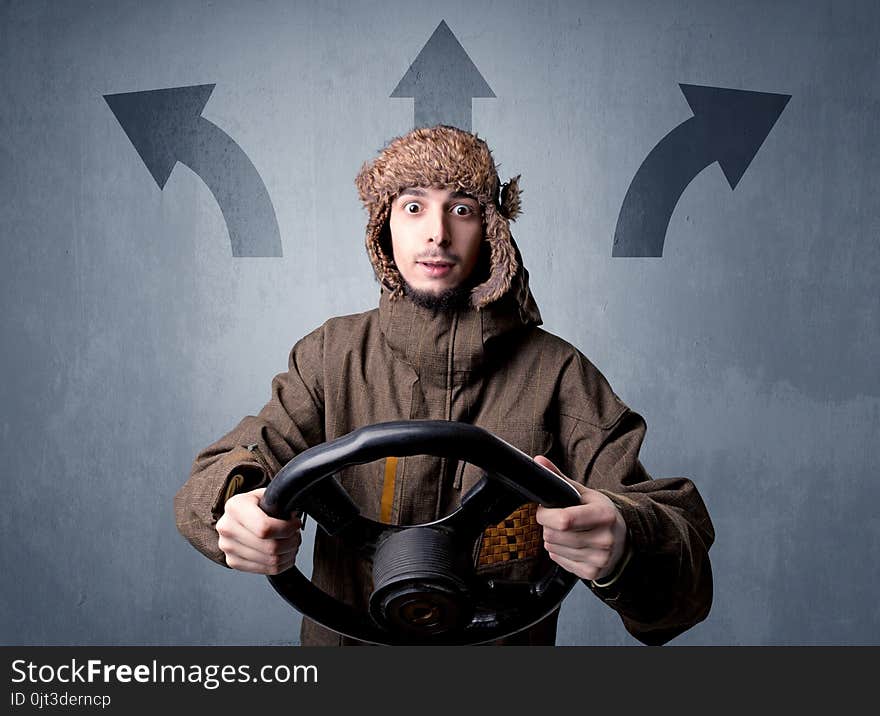 Young man holding black steering wheel with three arrows above his head pointing in different directions. Young man holding black steering wheel with three arrows above his head pointing in different directions