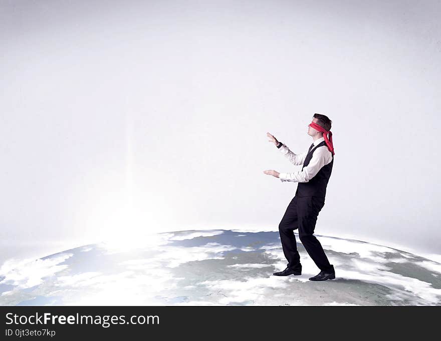 Young blindfolded businessman steps on a realistic globe. Young blindfolded businessman steps on a realistic globe