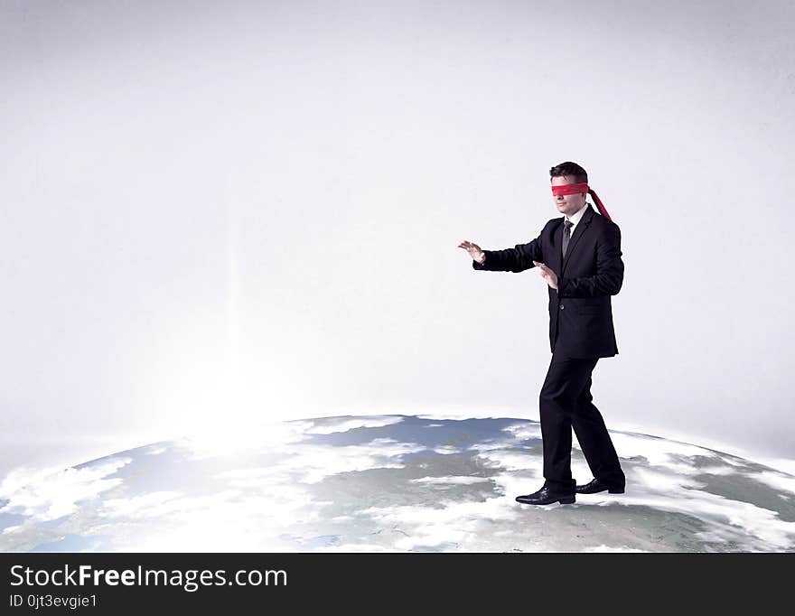 Young blindfolded businessman steps on a realistic globe. Young blindfolded businessman steps on a realistic globe