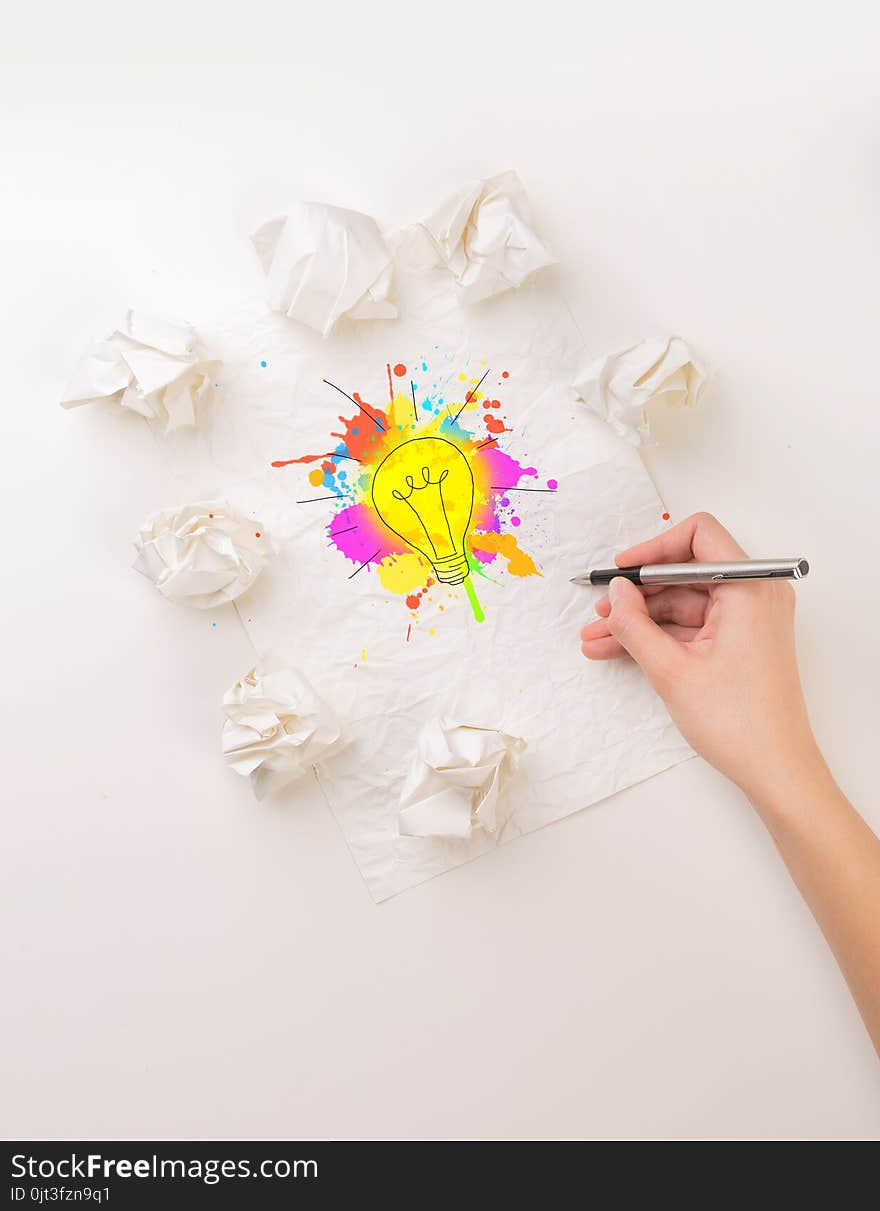 Female hand next to a few crumpled paper balls drawing a colorful lightbulb. Female hand next to a few crumpled paper balls drawing a colorful lightbulb