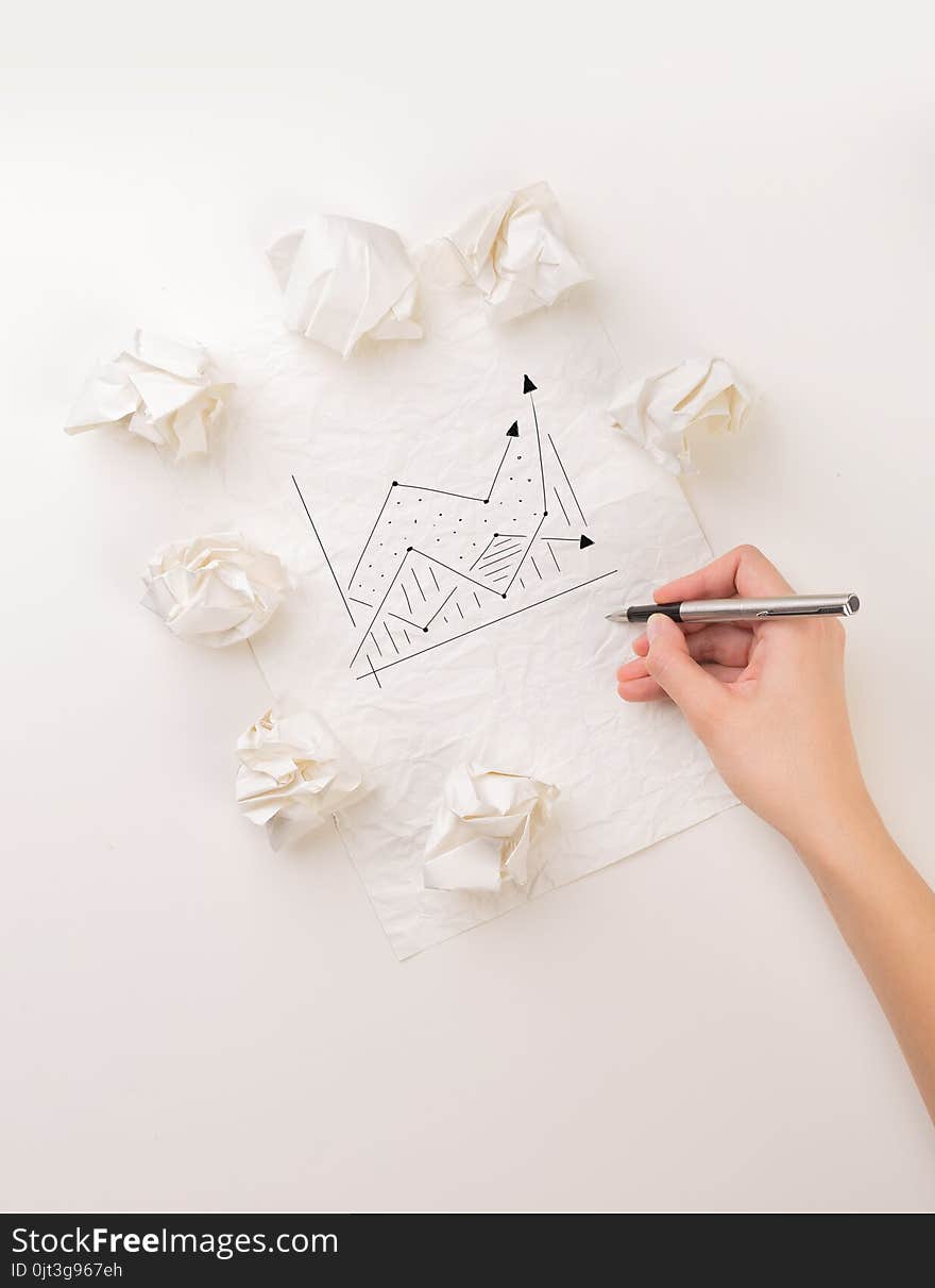 Female hand next to a few crumpled paper balls drawing a progress chart. Female hand next to a few crumpled paper balls drawing a progress chart