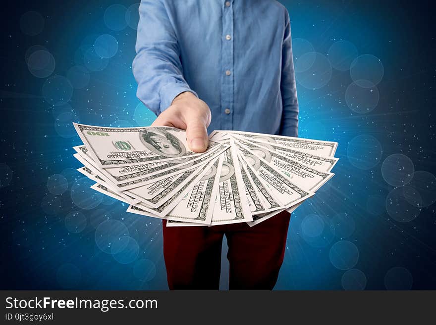 Young businessman holding large amount of bills with shiny blue background. Young businessman holding large amount of bills with shiny blue background