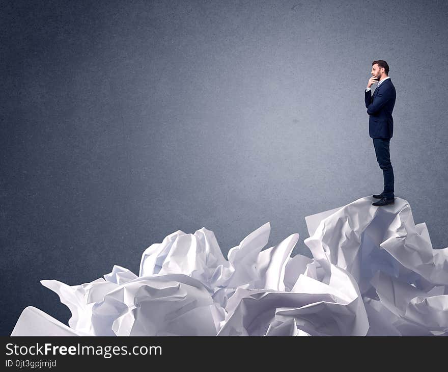 Thoughtful young businessman standing on a pile of crumpled paper. Thoughtful young businessman standing on a pile of crumpled paper