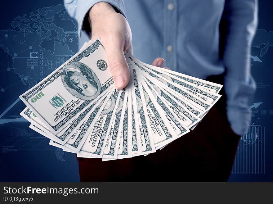 Young businessman holding large amount of bills with blue charts in the background. Young businessman holding large amount of bills with blue charts in the background