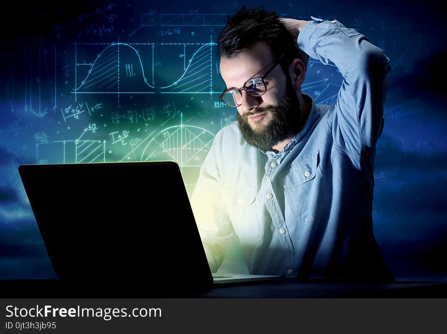 Young handsome businessman working late at night in the office with blue mathematic charts in the background. Young handsome businessman working late at night in the office with blue mathematic charts in the background