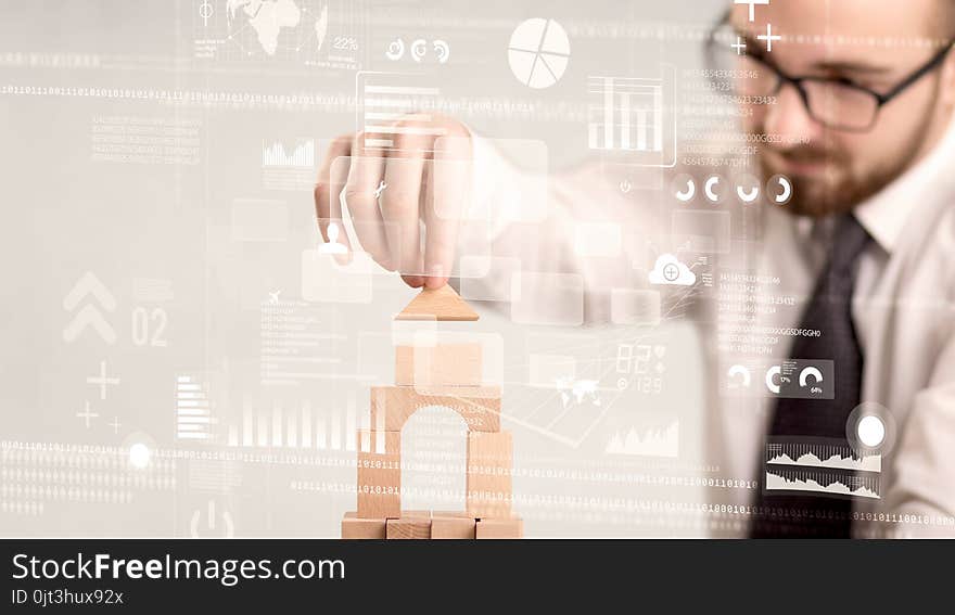 Young handsome businessman using wooden building blocks with mixed data around him. Young handsome businessman using wooden building blocks with mixed data around him