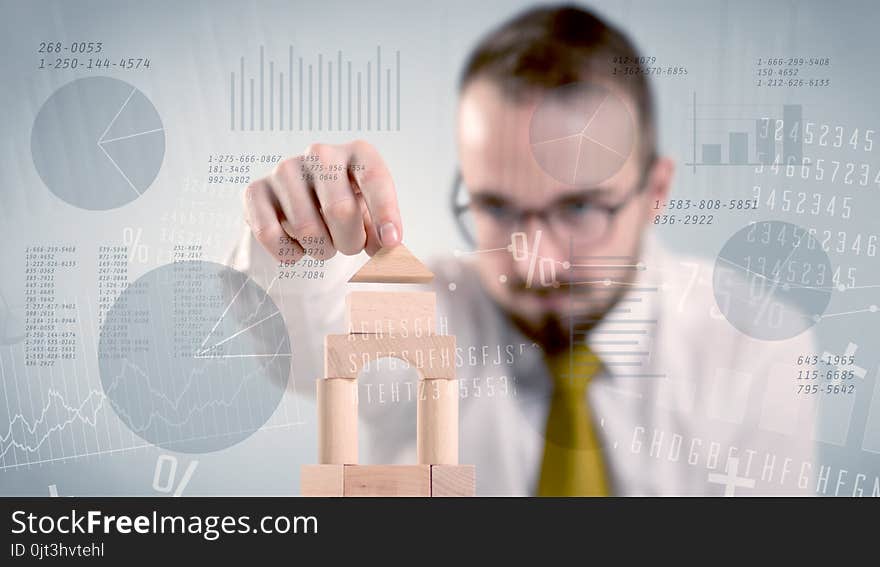 Young handsome businessman using wooden building blocks with data and numbers around him. Young handsome businessman using wooden building blocks with data and numbers around him