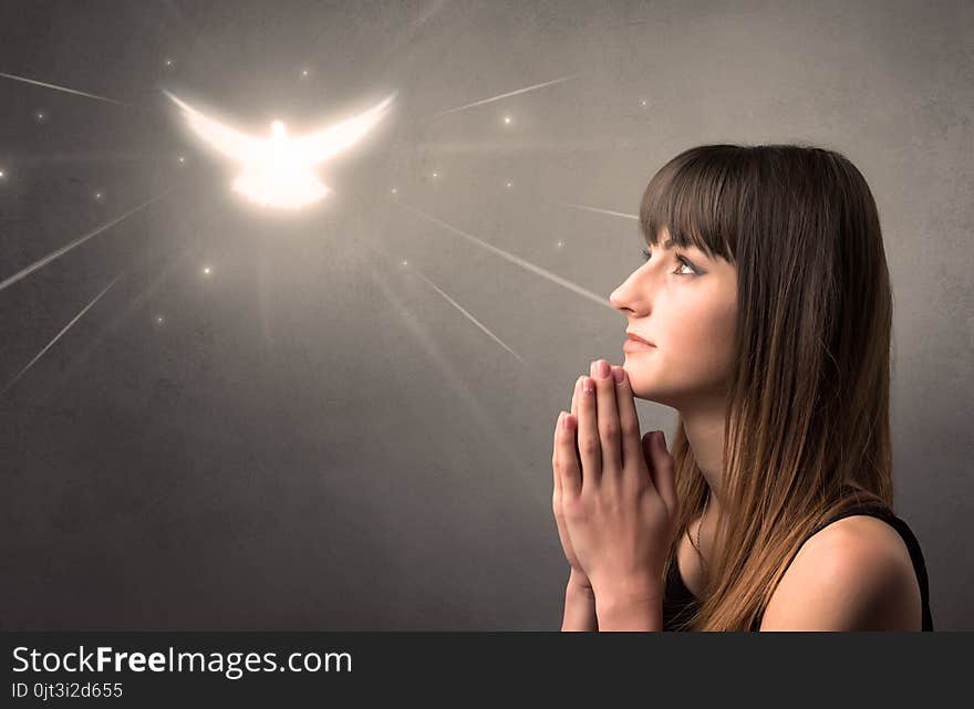 Young woman praying on a grey background with a sparkling bird above her. Young woman praying on a grey background with a sparkling bird above her