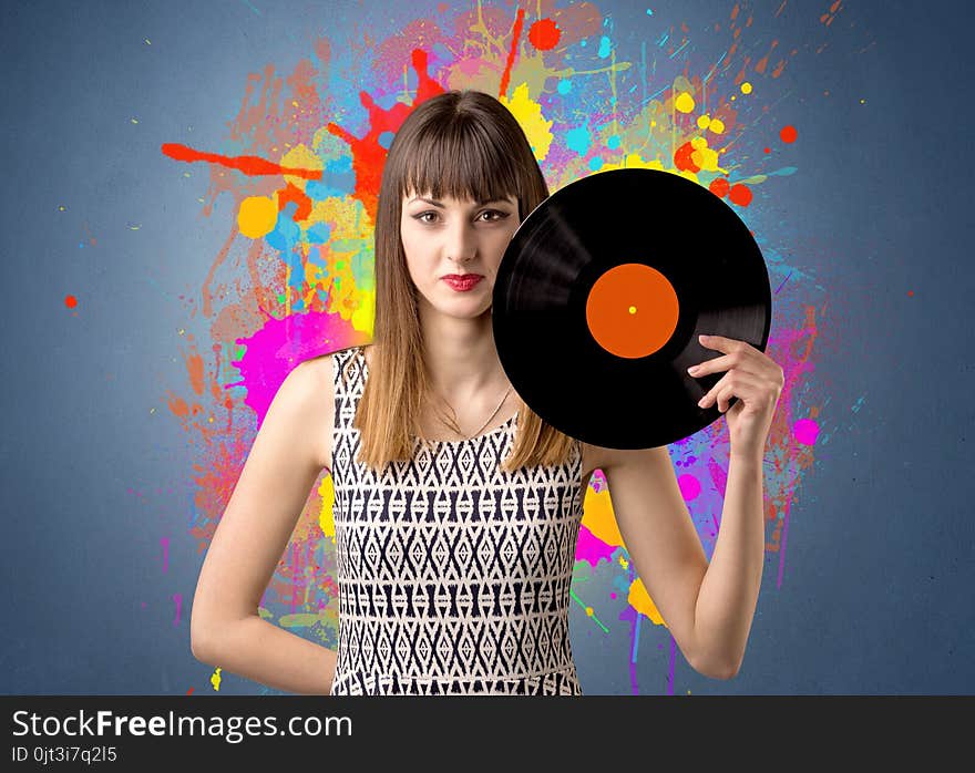 Young lady holding vinyl record on a grey background with colorful splashes behind her