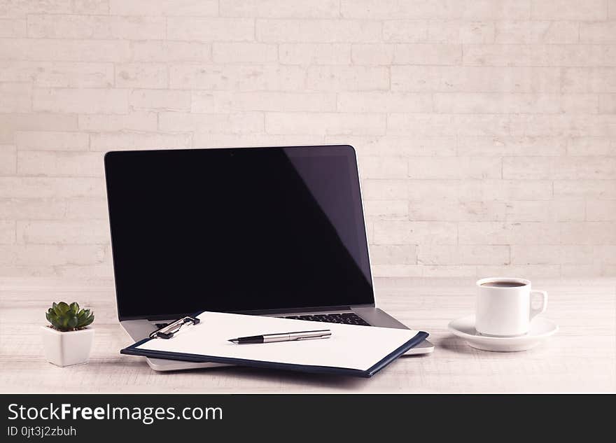 Close up of business office desk with pen board coffee in front of empty white brick textured wall background. Close up of business office desk with pen board coffee in front of empty white brick textured wall background.